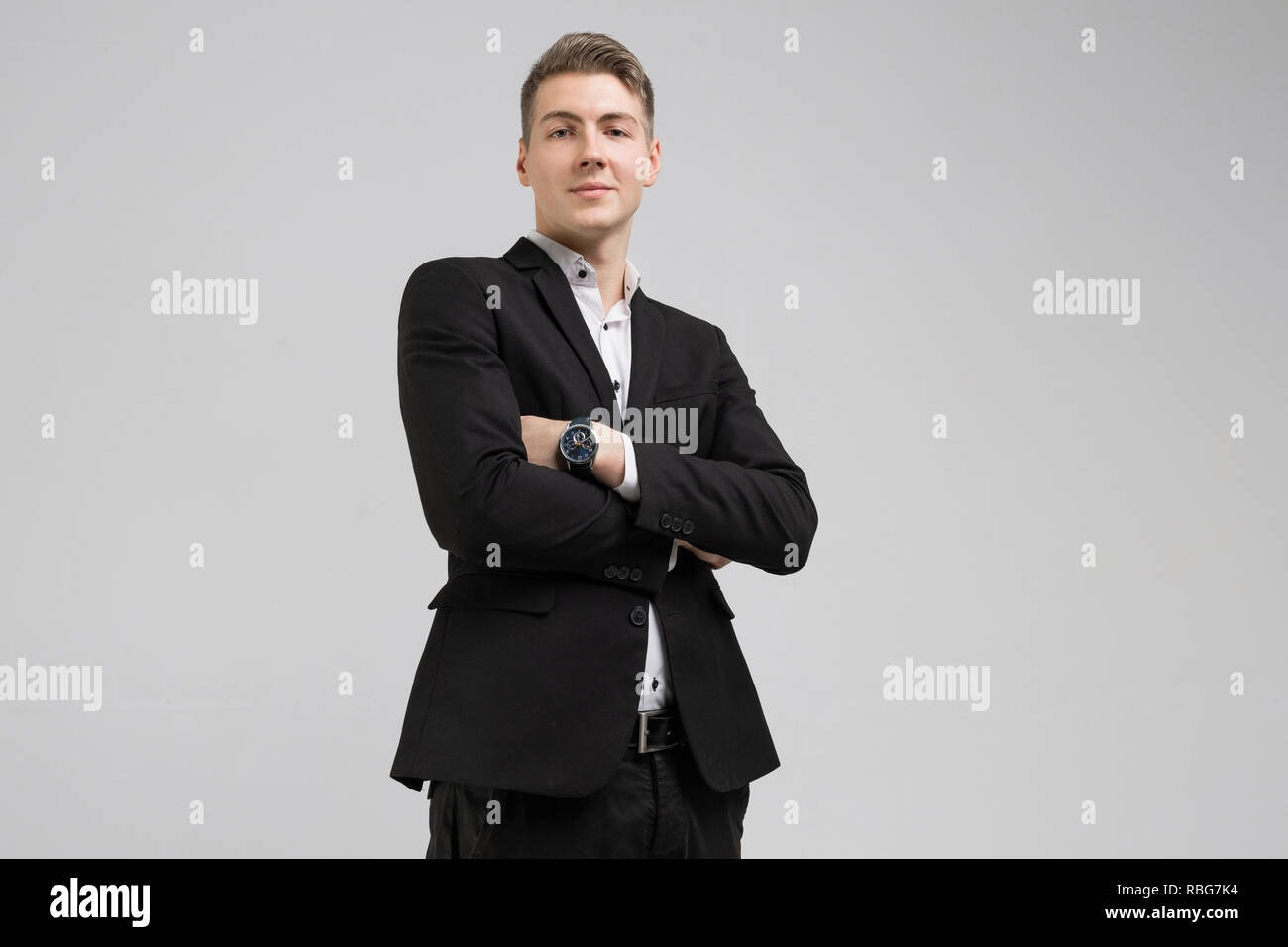 Portrait of young man in black suit with arms crossed isolated on white ...