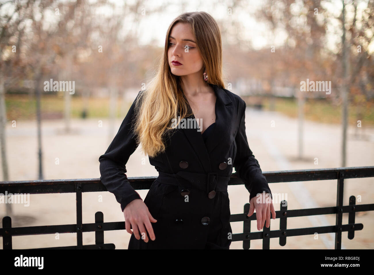 Pretty model woman posing in a park resting on a fence Stock Photo