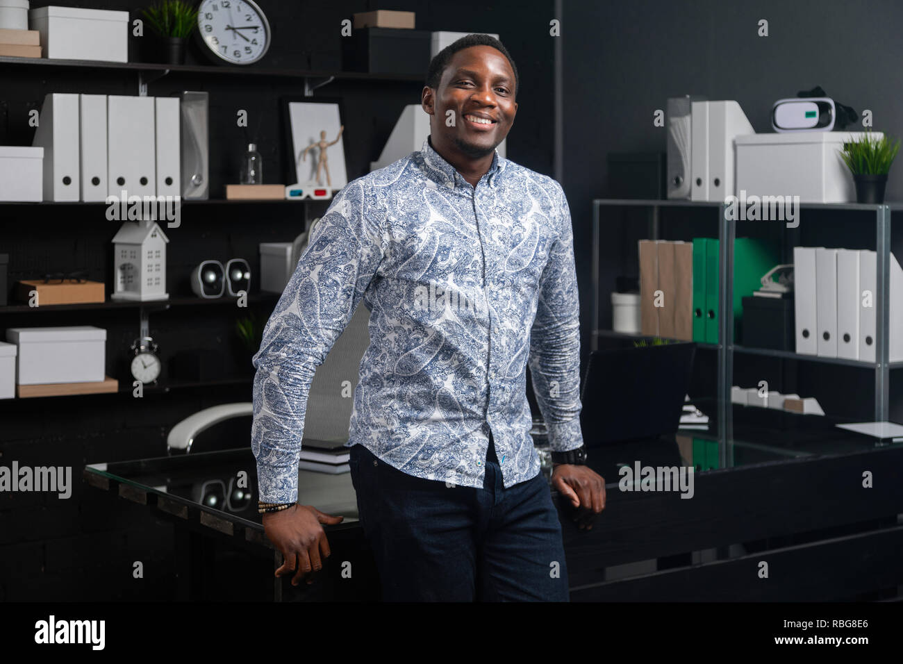 portrait of three-quarters long young black businessman standing near Desk in office Stock Photo