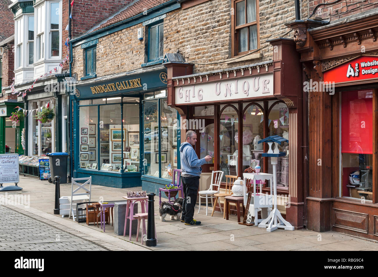 Bishop Auckland, County Durham, UK. A man looks at his mobile outside an art gallery and antique shop in the historic Fore Bondgate street Stock Photo