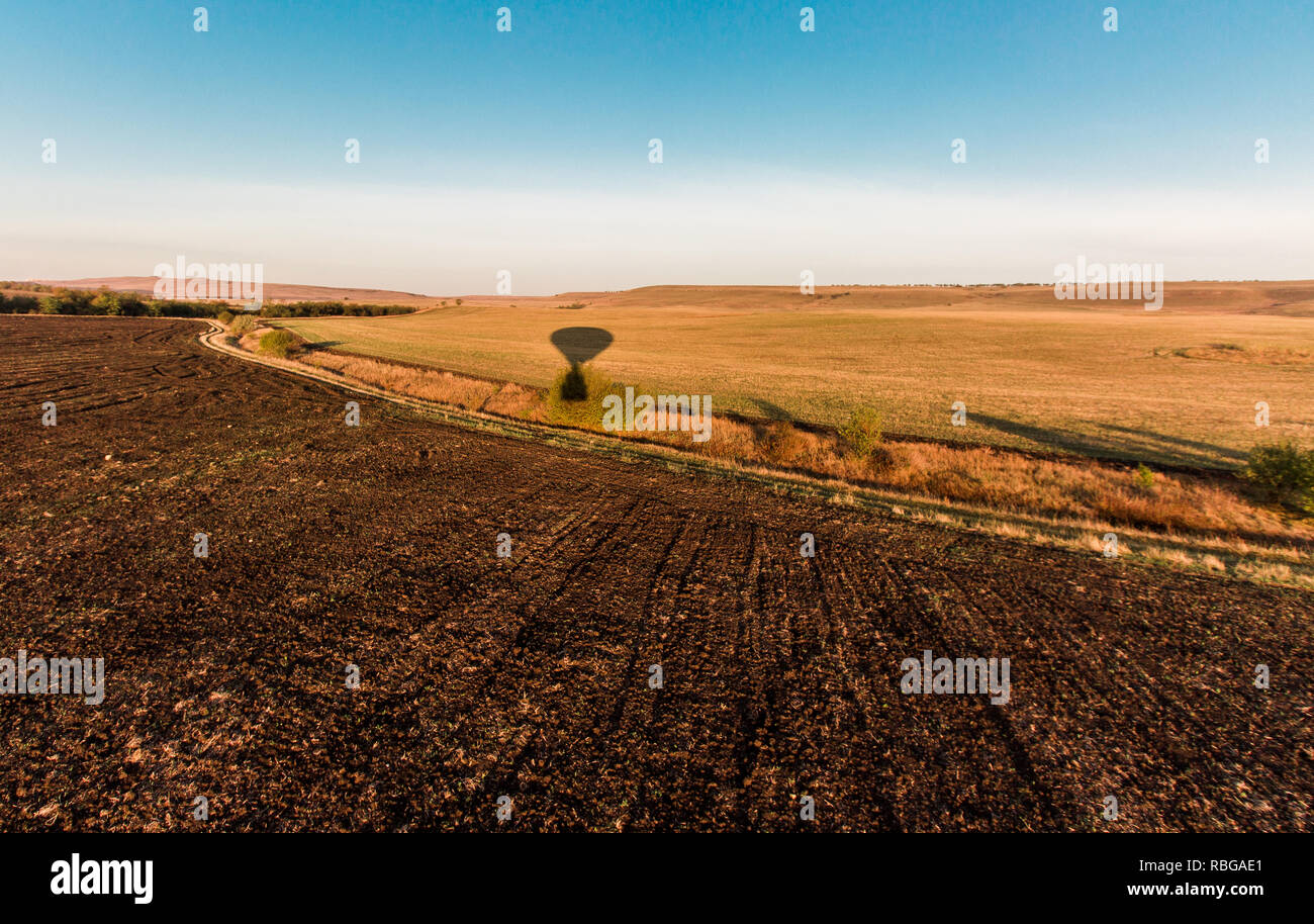 Hot air balloon shadow on the ground during sunrise flying over the ...