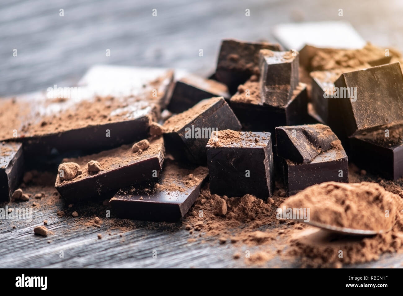 Pieces of dark bitter chocolate with cocoa powder on dark wooden