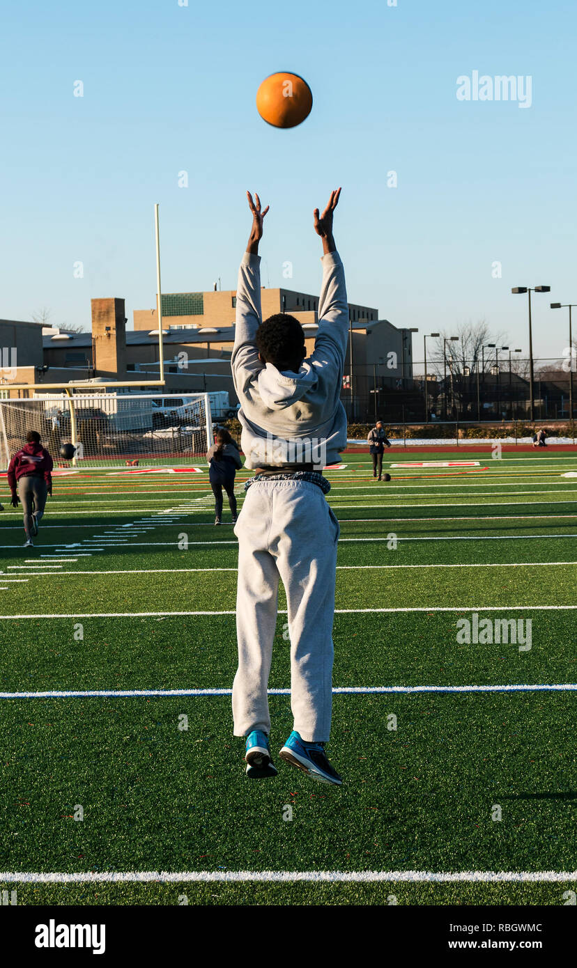 A male high school track and field athlete throwing a medicine ball in the air and jumping off of the ground during speed training drills. Stock Photo