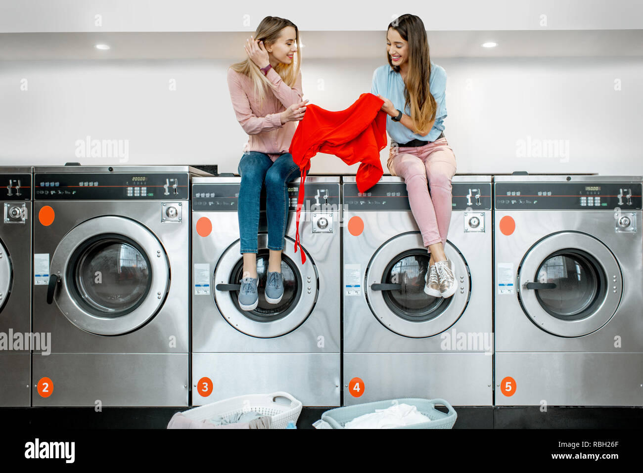 Two Cheerful Girlfriends Sorting Clothes For Washing Sitting On The