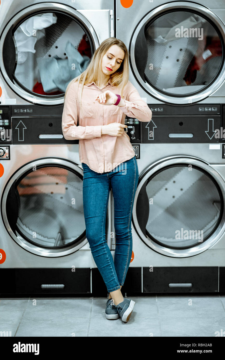 Young woman standing near the dryer machines waiting for clothes to be dried in the self serviced laundry Stock Photo