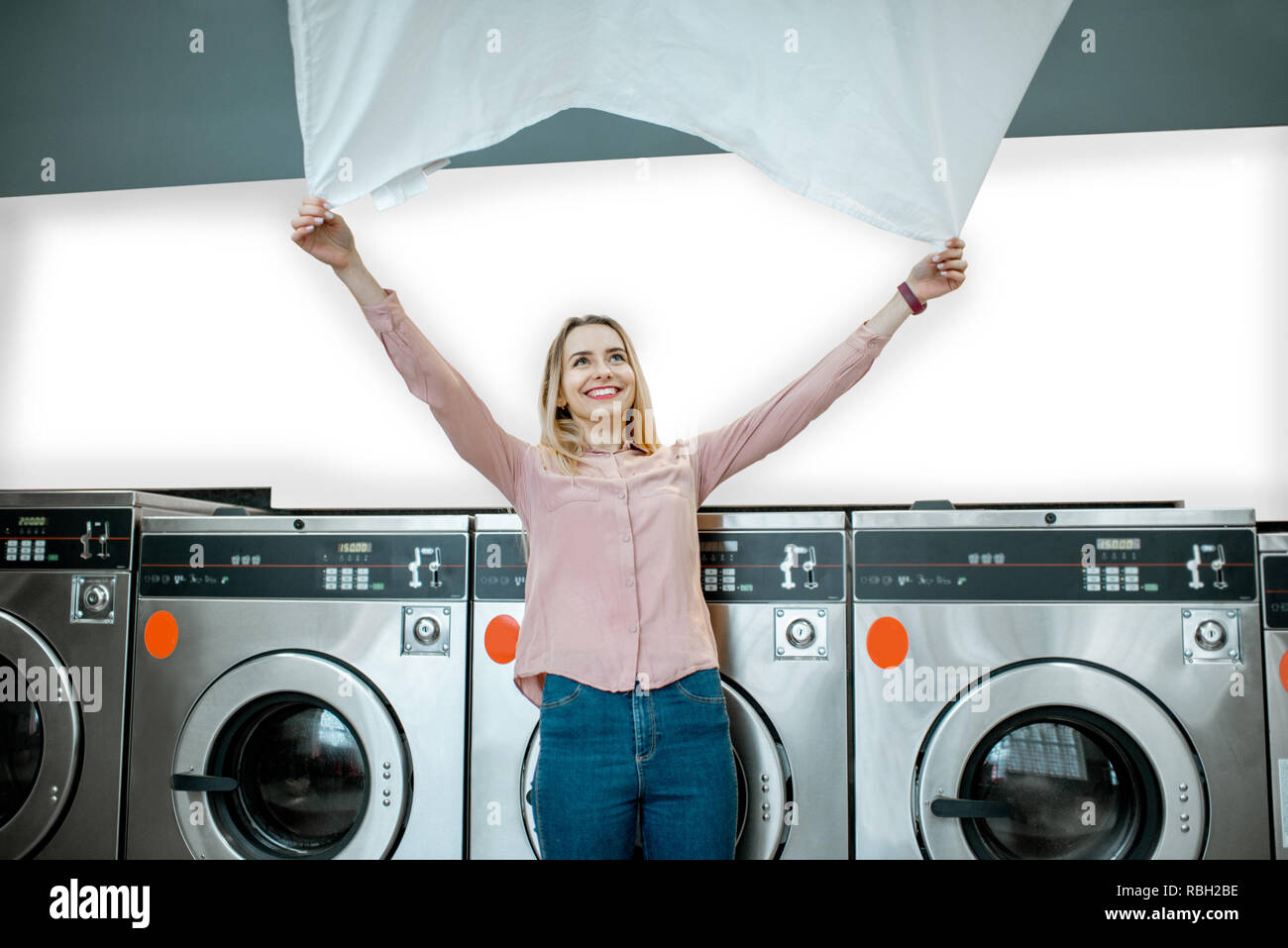 Young woman throwing up a bedsheet making clothes after the washing in the public laundry Stock Photo