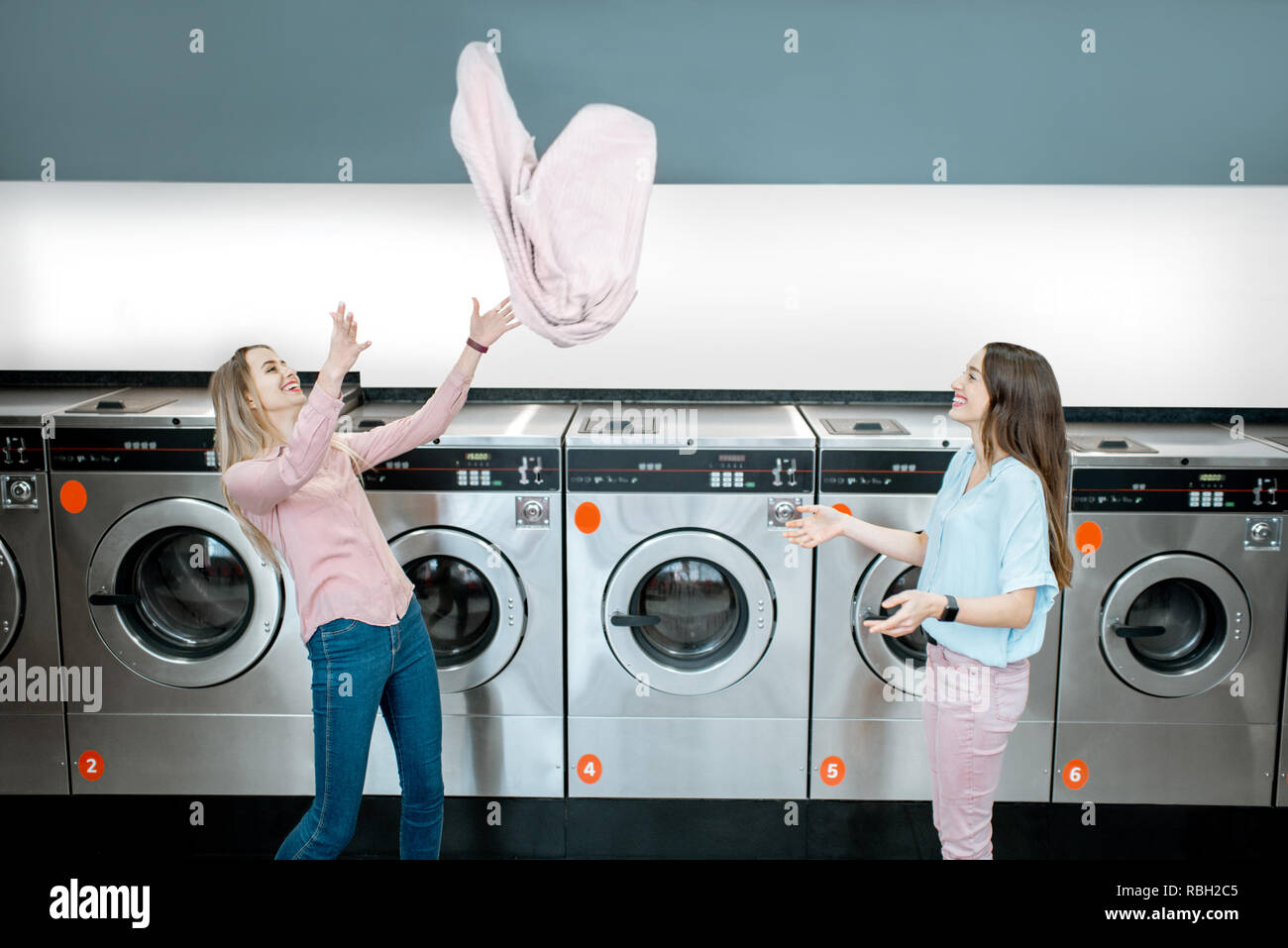 Young and playful women throwing up a towel making clothes after the washing in the public laundry Stock Photo