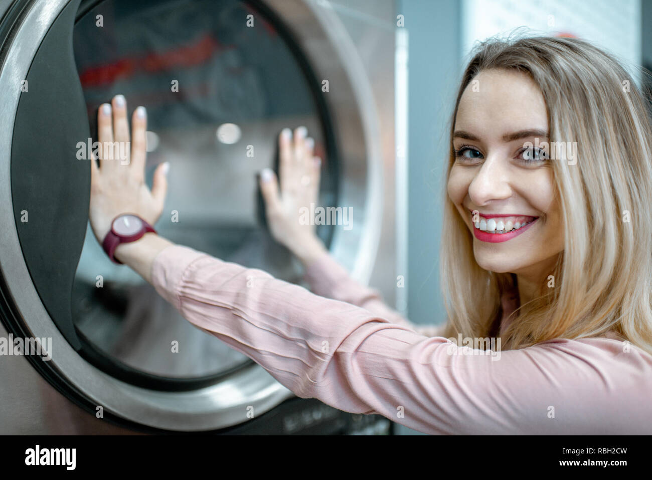 Young and cheerful woman enjoying the washing process standing near professional drying machine in the laundry Stock Photo