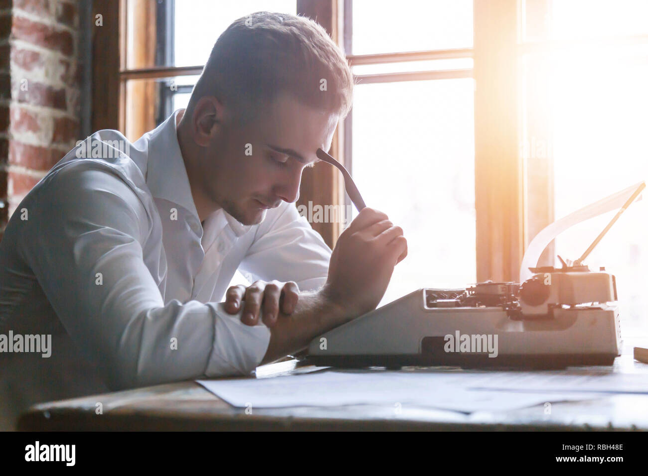 This man write. Мужчина в светлой рубашке грустно задумался возле стола в офисе.