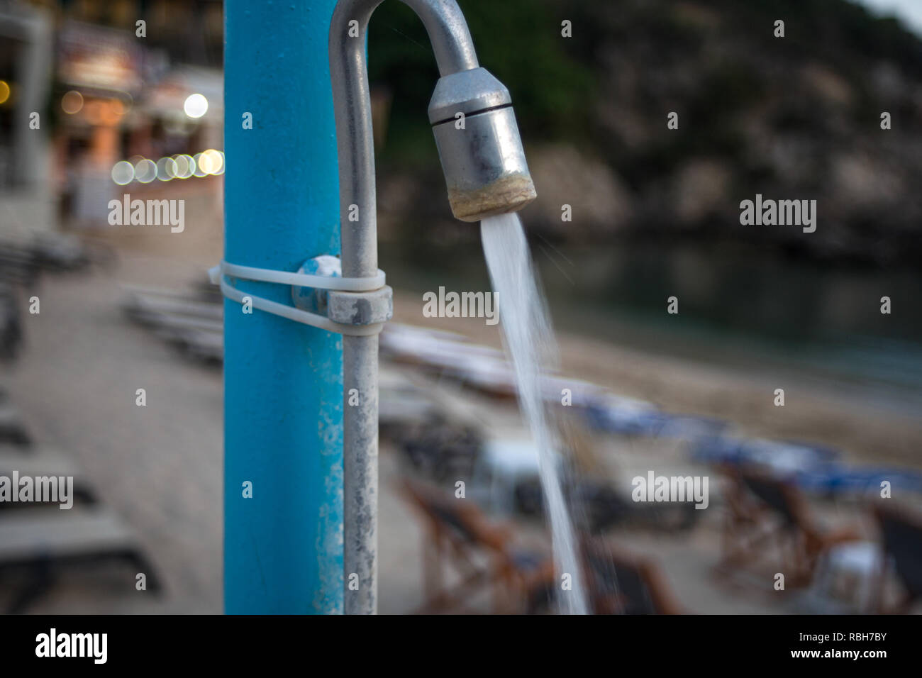 Water Pouring from Weathered Shower Head. Pipe Tied to Pole by Plastic