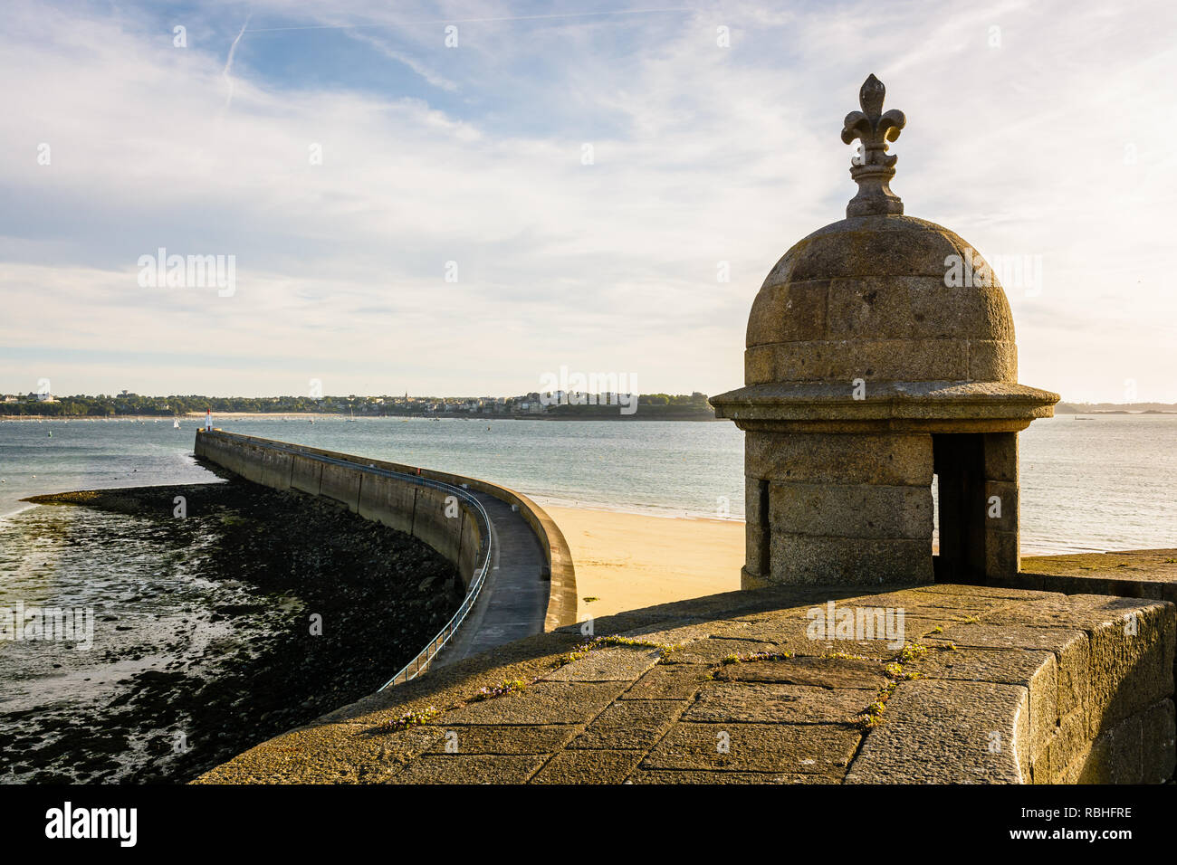 The breakwater of the old town of Saint-Malo in Brittany, seen at low tide and sunset from the city wall, with a granite turret in the foreground. Stock Photo