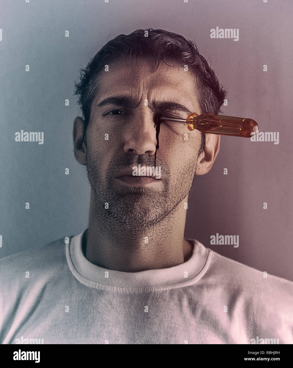 A man looking at the camera while the blood slips from his eye due to a screwdriver. Stock Photo