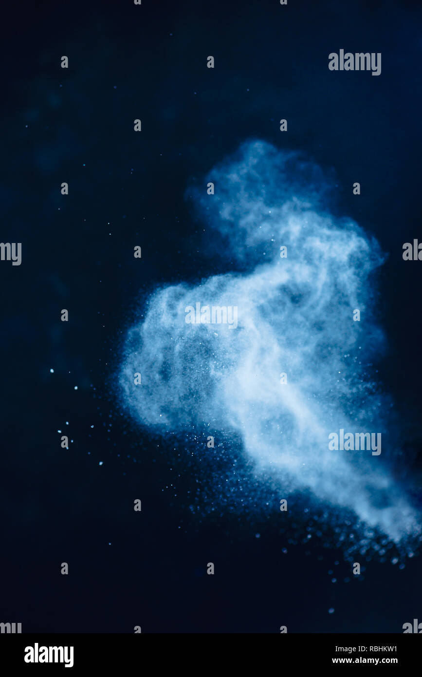 Flour powder explosion in motion. Action food photography. Light blue dust on a black background