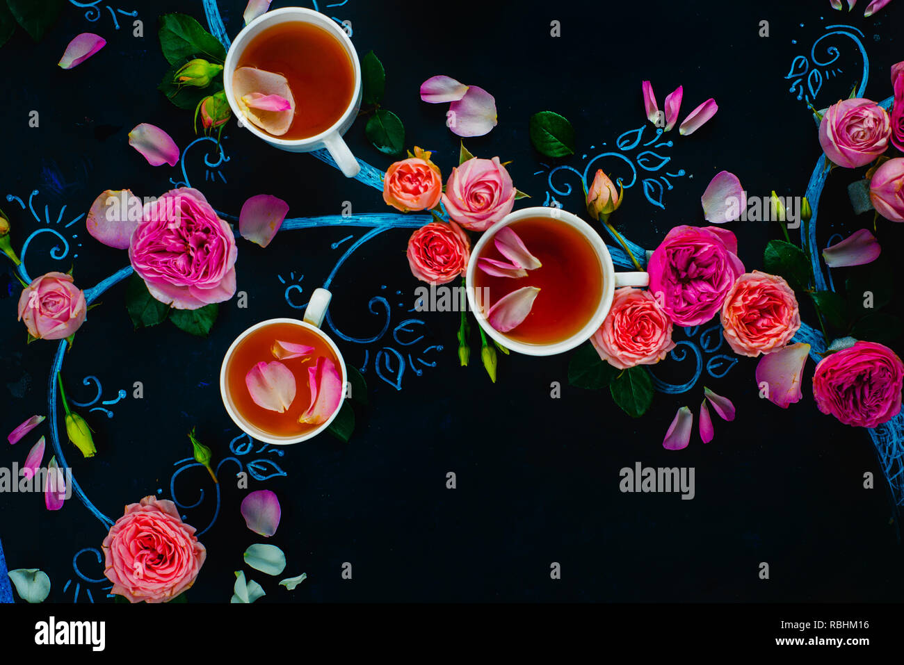 Teacups and flower petals in chalk tree flat lay. Rose tea creative flat lay on a dark background with copy space Stock Photo