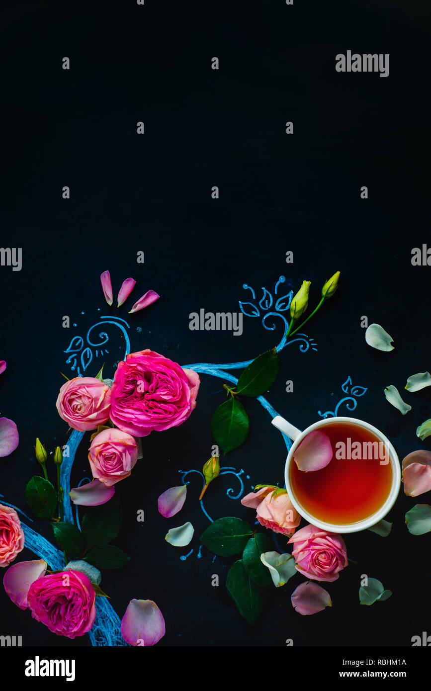 Teacups and flower petals in chalk tree flat lay. Rose tea creative flat lay on a dark background with copy space Stock Photo