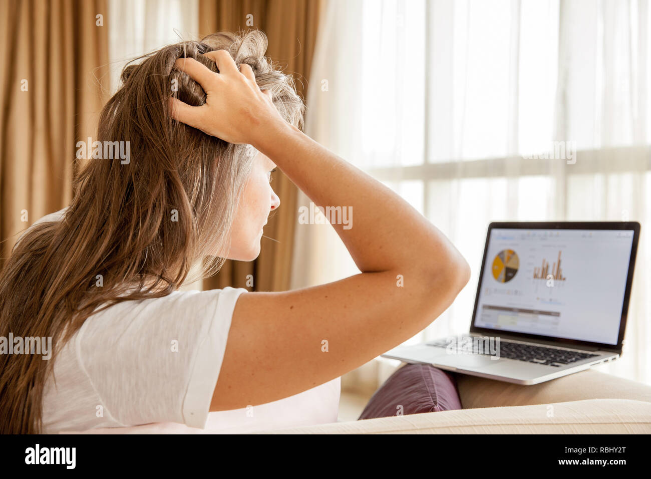 Woman is pulling her hair in frustration reading financial report on her laptop Stock Photo