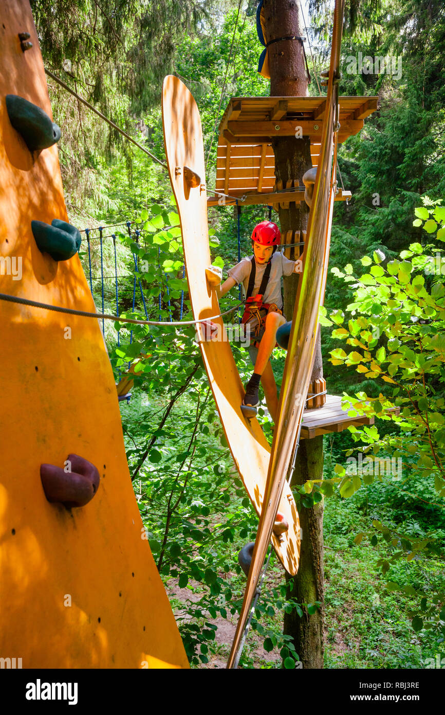 Teenager boy wearing safety harness passing rope bridge obstacle at a ropes course in outdoor treetop adventure park Stock Photo