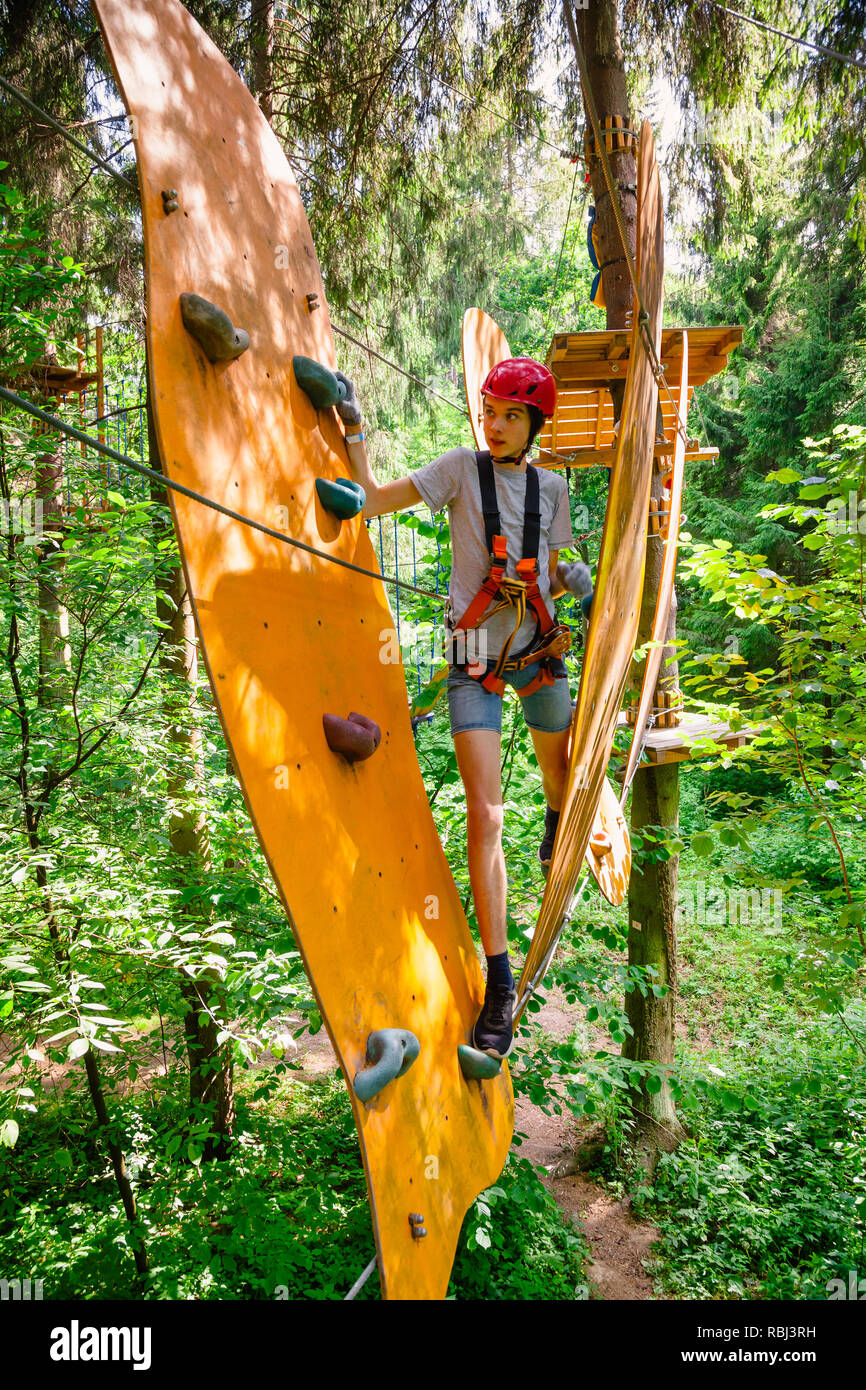 Teenager boy wearing safety harness passing rope bridge obstacle at a ropes course in outdoor treetop adventure park Stock Photo