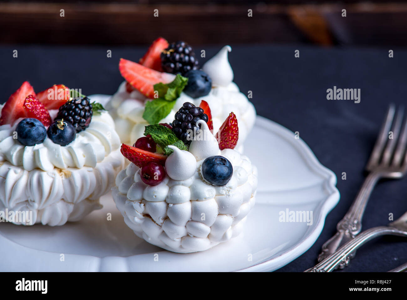 Delicate white meringues with fresh berries on the plate. Dessert Pavlova close-up. Dark background. A festive wedding cake. Stock Photo