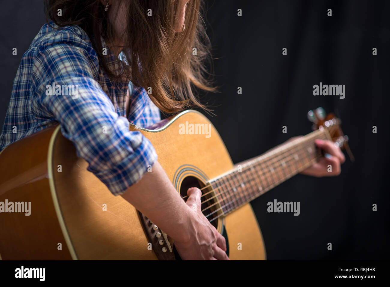 The girl teenager playing an acoustic guitar on a dark background in ...