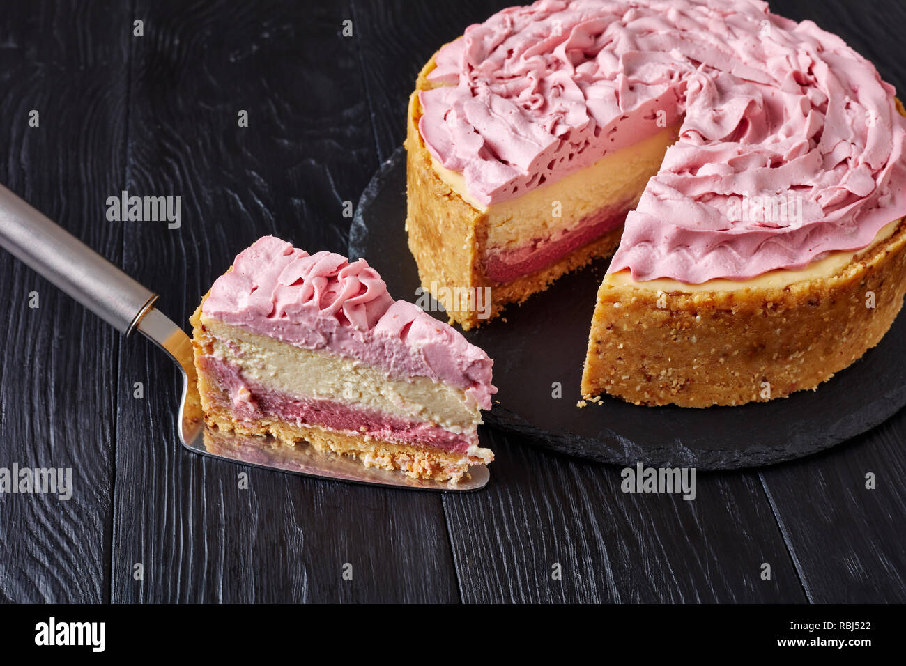 raspberry layered cheesecake topped with cream cheese coloured with ground raspberries sliced on a black stone tray on wooden table, view from above, Stock Photo
