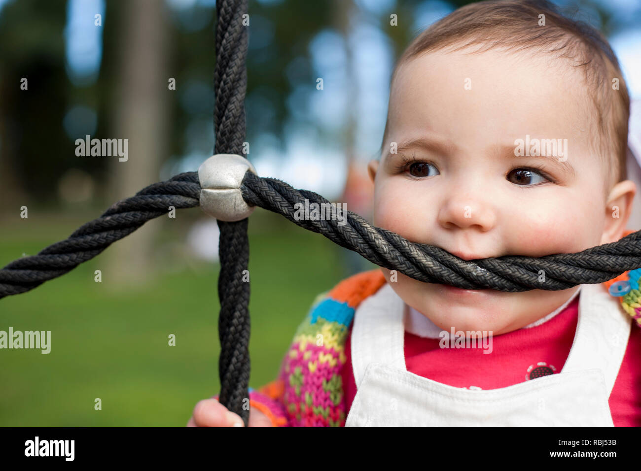 11 month baby girl biting playground rope as it was a teether. Biting and Teething for babies concept Stock Photo