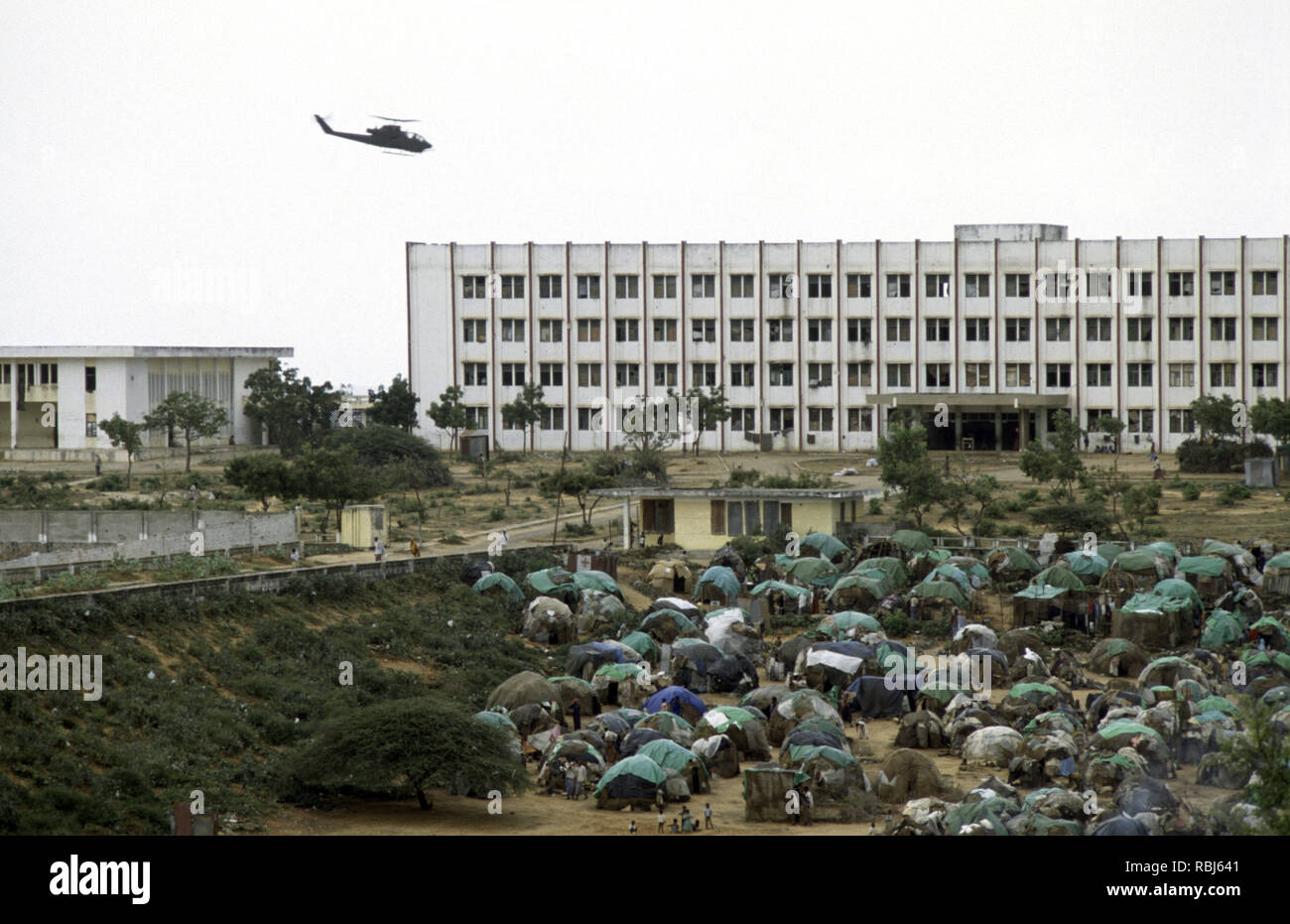 10th October 1993 A U.S. Army Bell AH-1 Cobra attack helicopter patrols low above a tented refugee camp in front of the Polytechnic Institute in Mogadishu, Somalia. Stock Photo