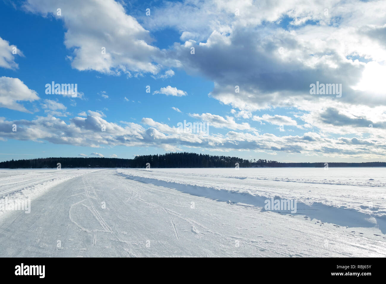 Slippery road on the ice of frozen lake on a sunny winter day in Finland. White snow and clouds on blue sky.Beautifull winter landscape. Stock Photo