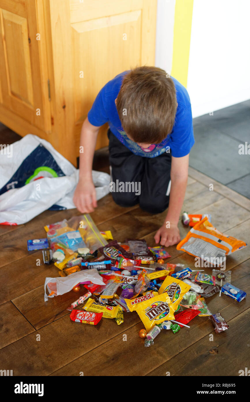 A six year old boy kneeling on the floor surrounded by sweets he has been given trick or treating at Halloween in Quebec, Canada Stock Photo