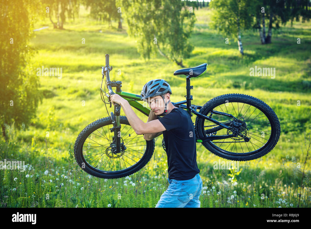 Cyclist man in helmet carries his mountain bike in the rise in the background green nature. Concept of active and healthy lifestyle Stock Photo
