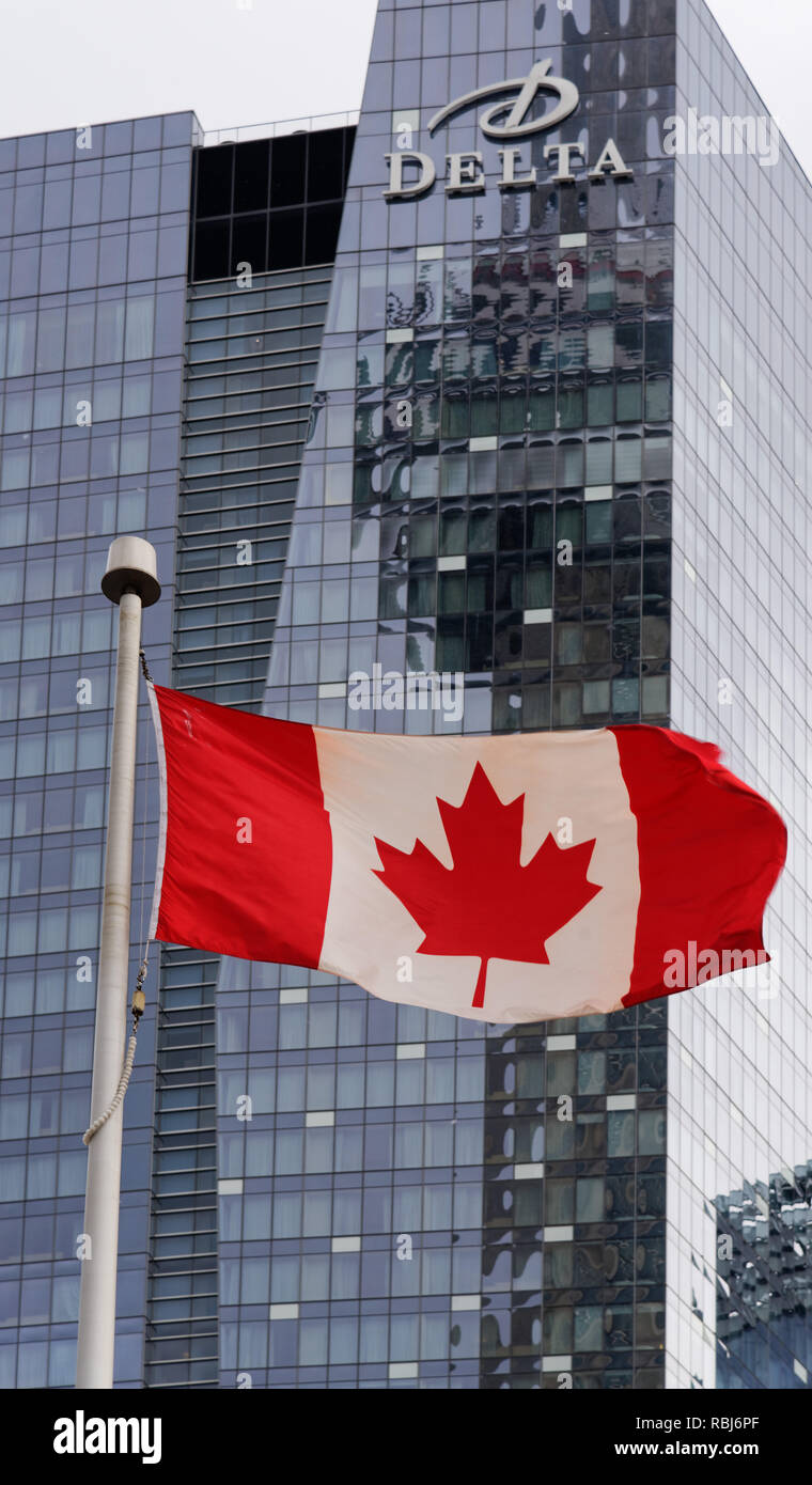 The CN Tower reflected in the Hotel Delta building in Toronto, with the Canadian flag flying in front Stock Photo