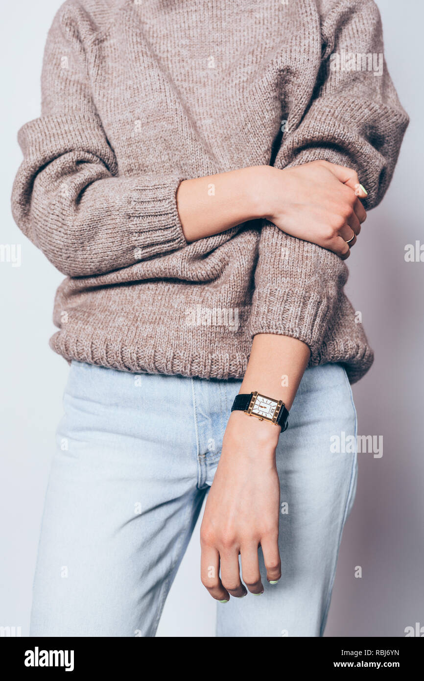 Stylish young woman wearing plain brown oversized sweater and boyfriend jeans posing on white background, close-up. Stock Photo