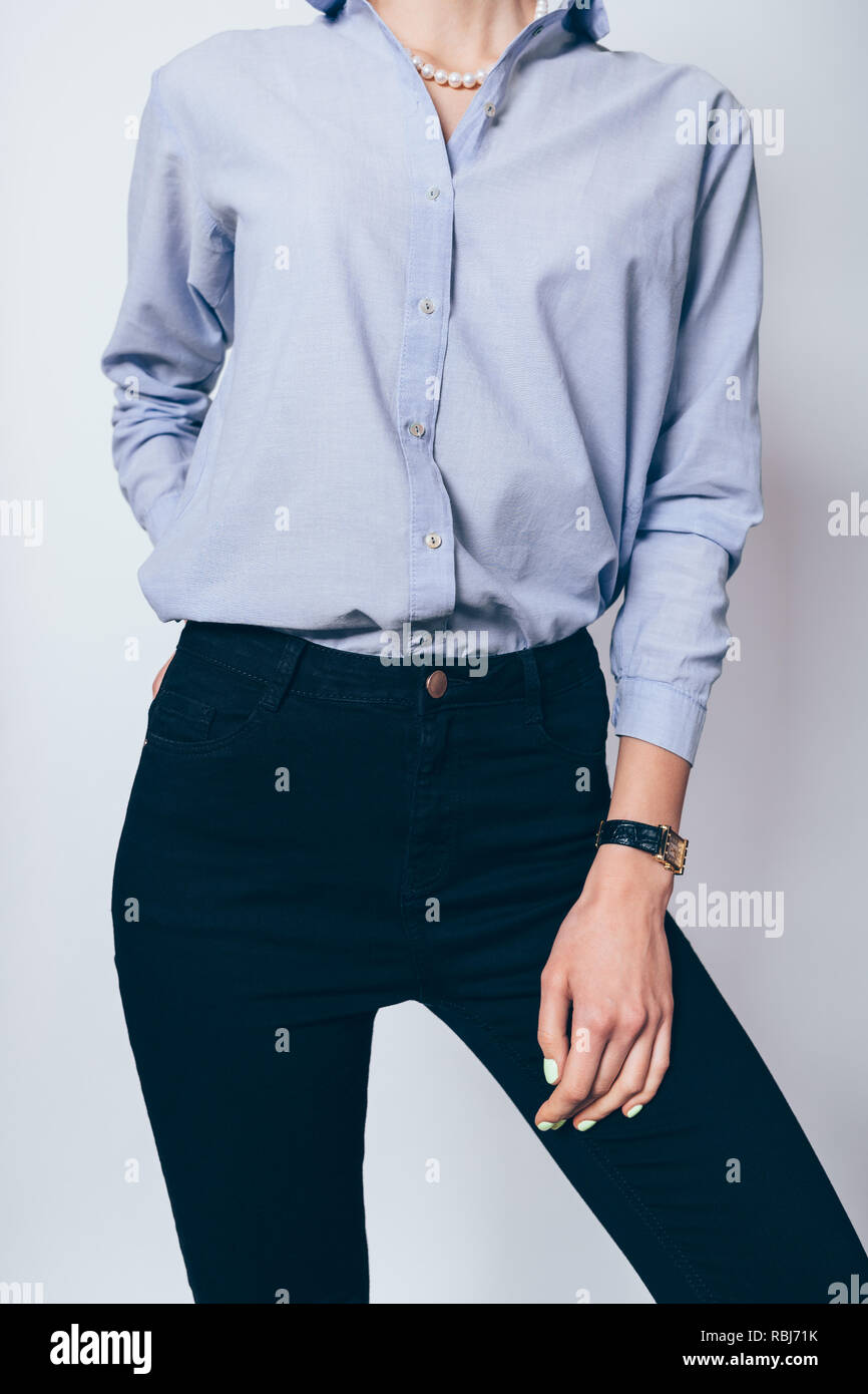Close-up of young woman wearing blue shirt and tight black pants standing on white background. Stock Photo