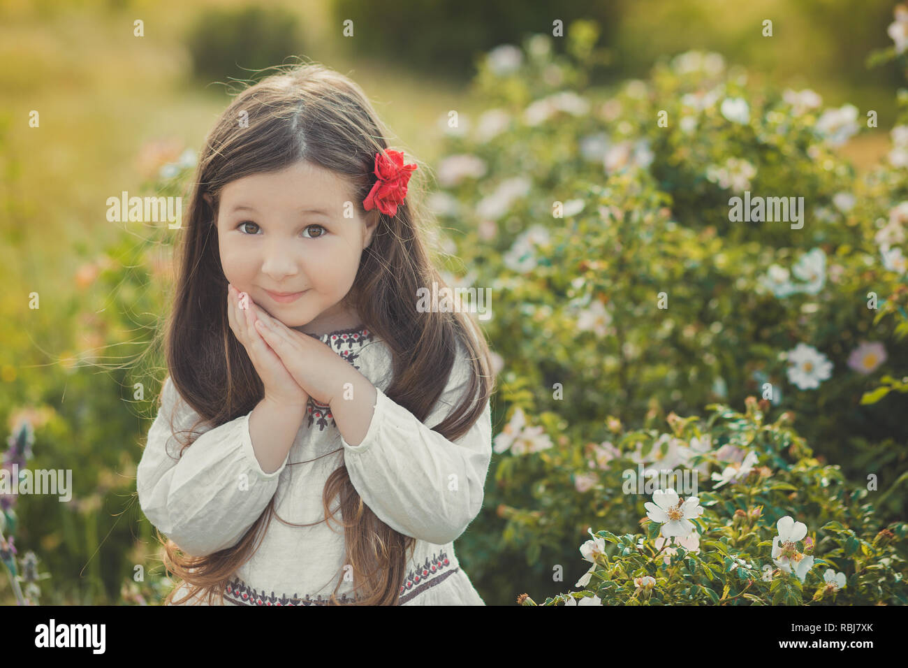 Girl with brunette hair and brown eyes stylish dressed wearing rustic village clothes white shirt and red pants on belt posing with flowers in forest  Stock Photo