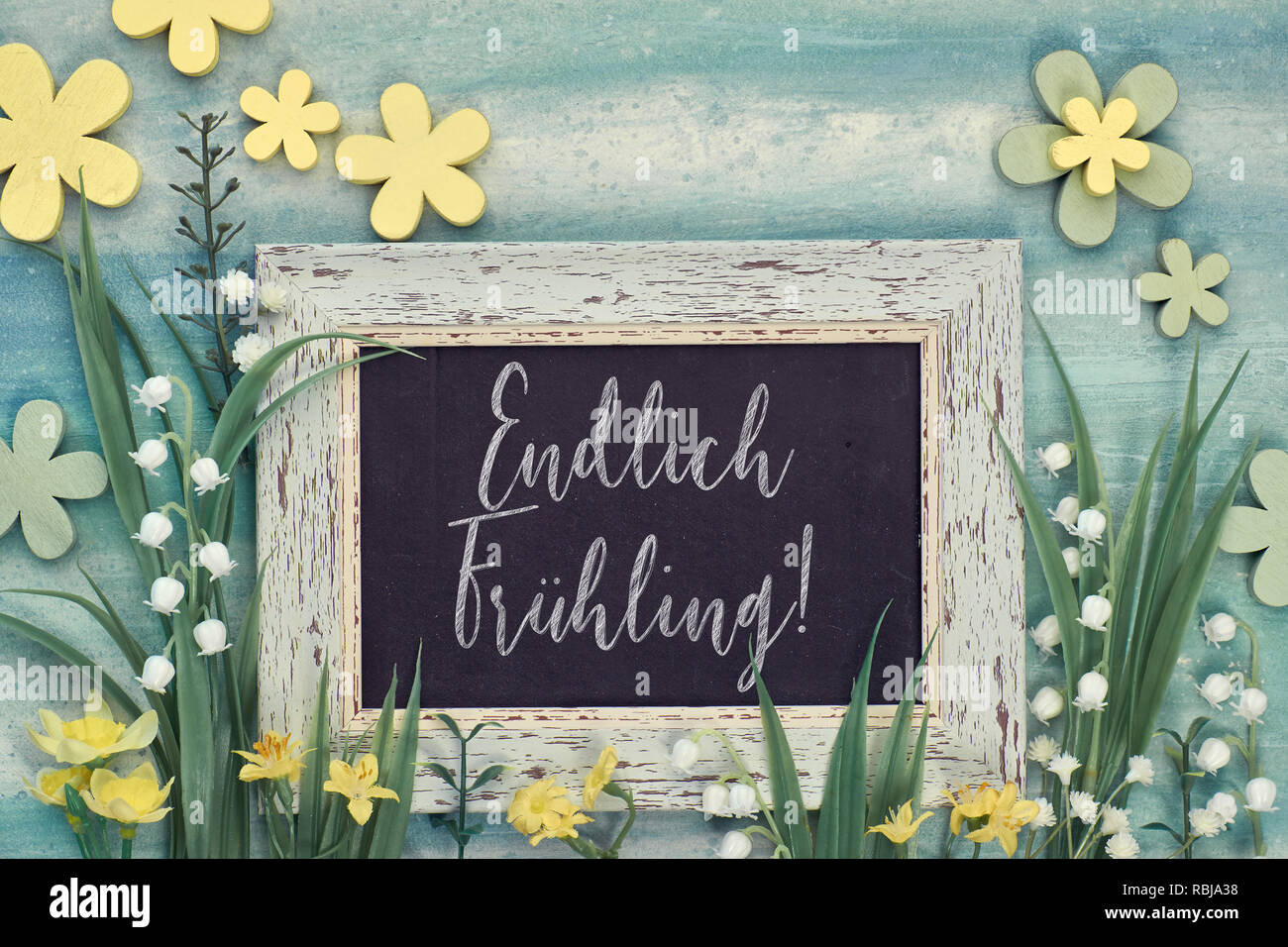 Spring background: blackboard framed with spring flowers on green textured background. Chalk text on the board "Endlihc fruhling" means "Finallz Sprin Stock Photo