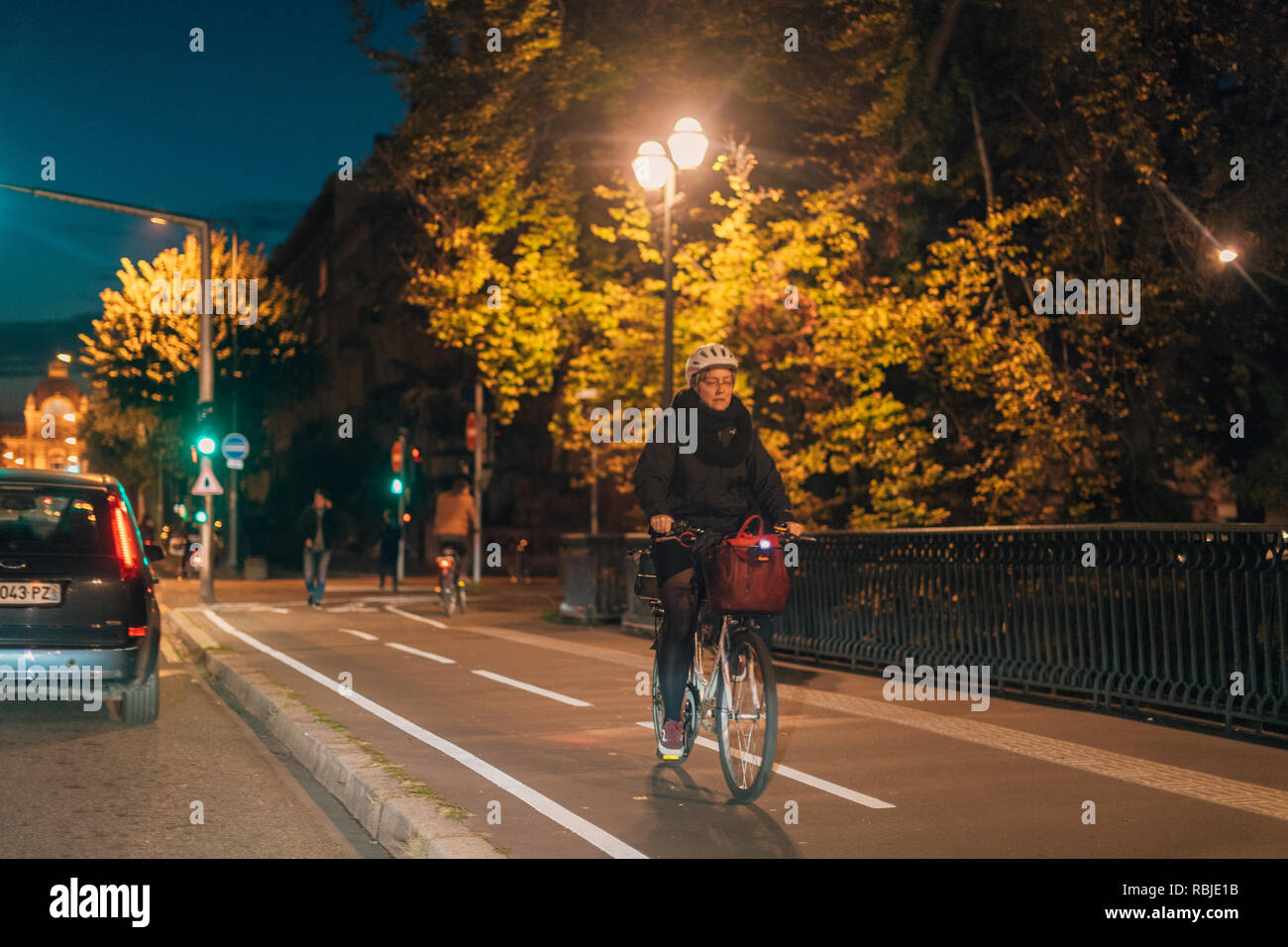 STRASBOURG, FRANCE - OCT 31, 2017: Senior woman riding a bike at night in central Strasbourg going home - wearing protection helmet  Stock Photo