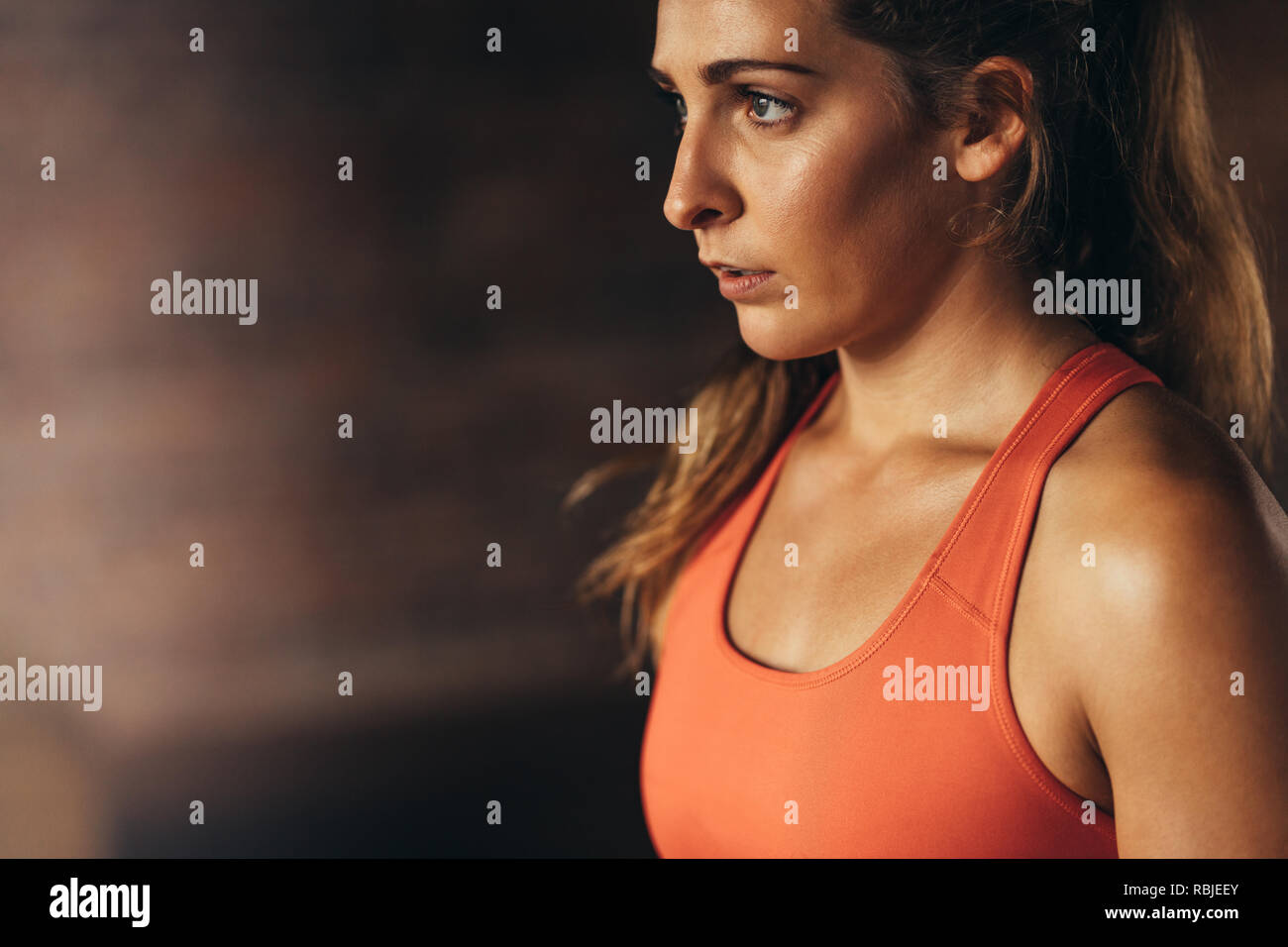 Close up of young woman in orange sports bra looking away. Female taking break after workout. Stock Photo