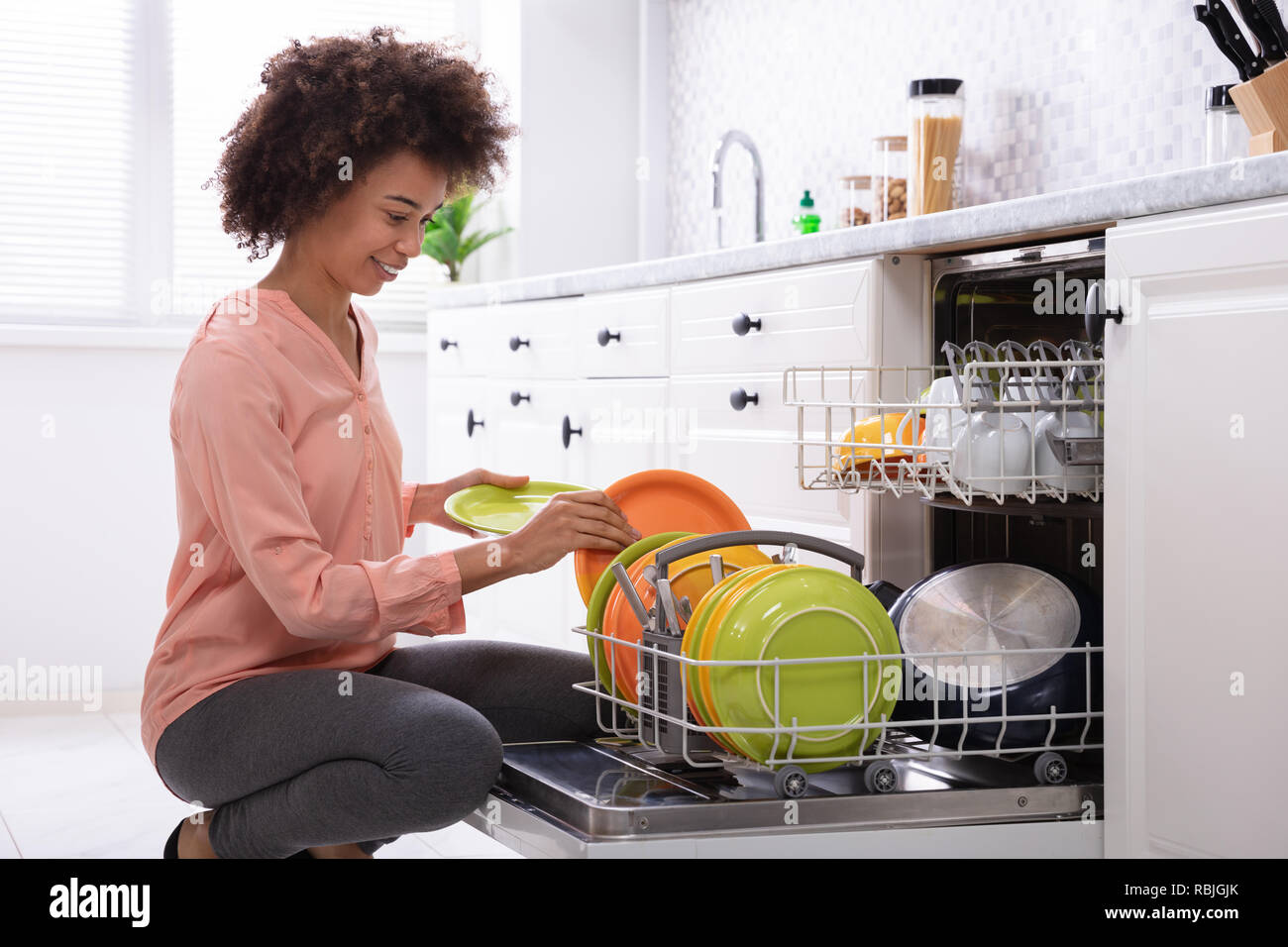 https://c8.alamy.com/comp/RBJGJK/smiling-young-woman-crouching-on-floor-arranging-plates-in-dishwasher-at-modular-kitchen-RBJGJK.jpg