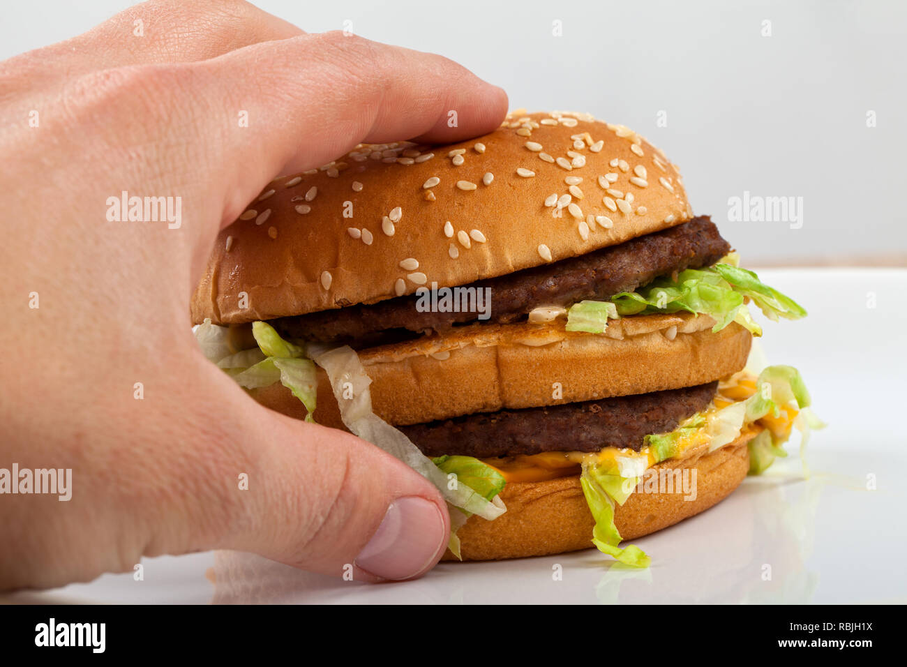 Close up picture of human hand holding a tasty double cheeseburger with lettuce Stock Photo