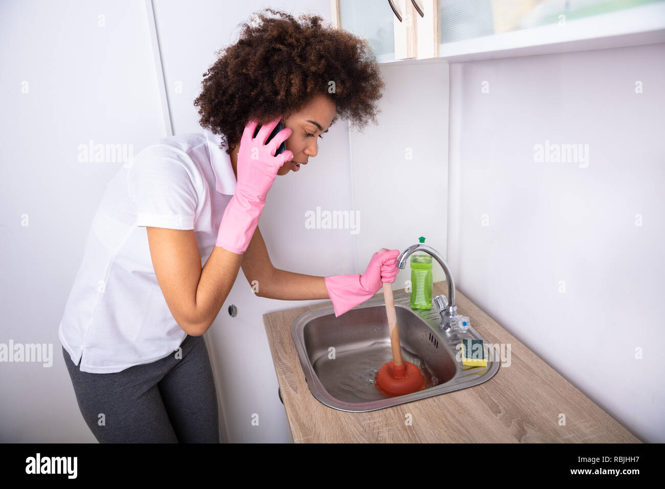 Closeup Of A Woman Calling Plumber On Mobile Phone While Cleaning The