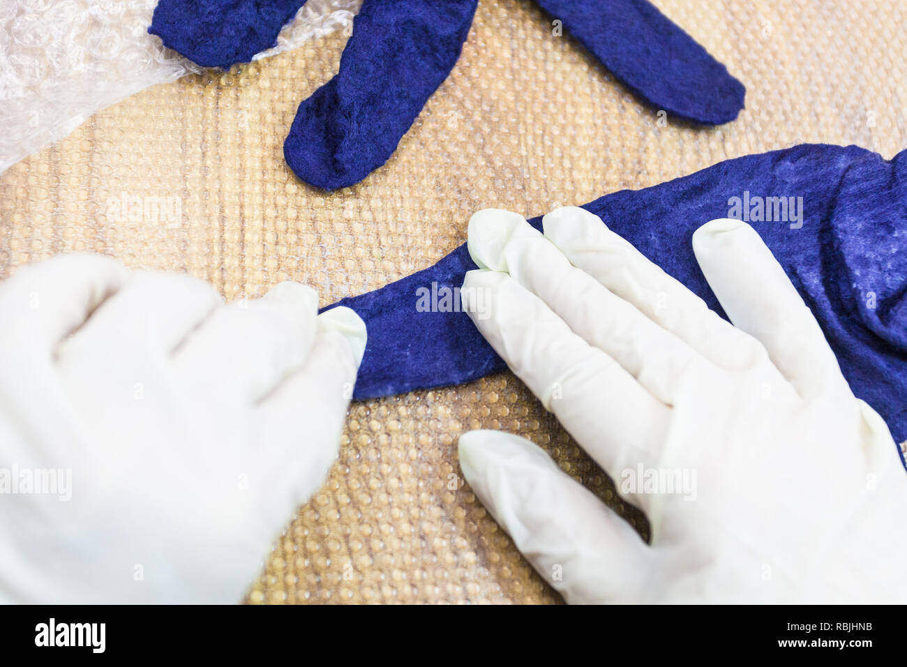 workshop of hand making a fleece gloves from blue Merino sheep wool using wet felting process - craftsman condensing fingers of the felted glove Stock Photo