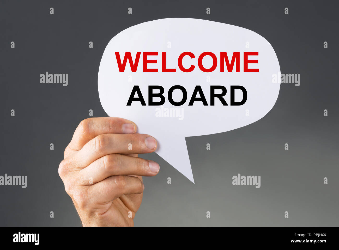 A Person's Hand Holding Welcome Aboard Thought Bubble On Grey Background Stock Photo