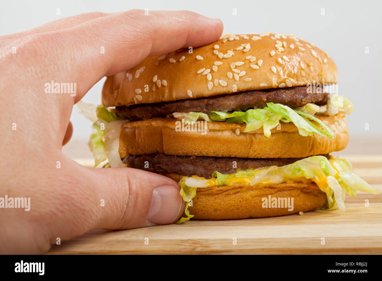 Close up picture of human hand holding a tasty double cheeseburger with beef, cheddar and lettuce Stock Photo