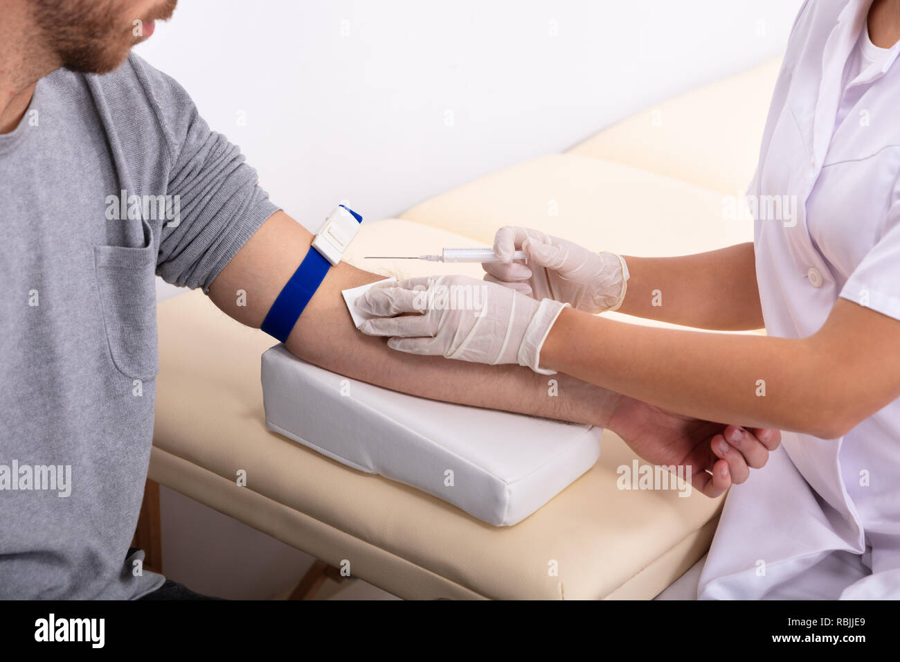 Young Female Doctor Injecting Male Patient With Syringe To Collect 