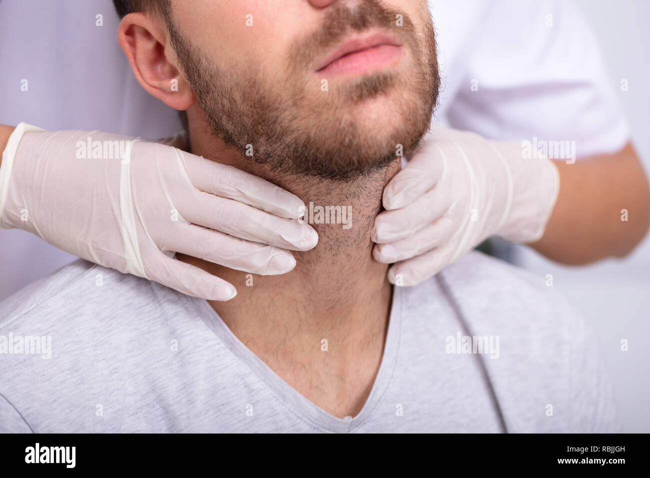 Doctor's Hand Wearing Gloves Performing Physical Exam Palpation Of The Thyroid Gland Stock Photo