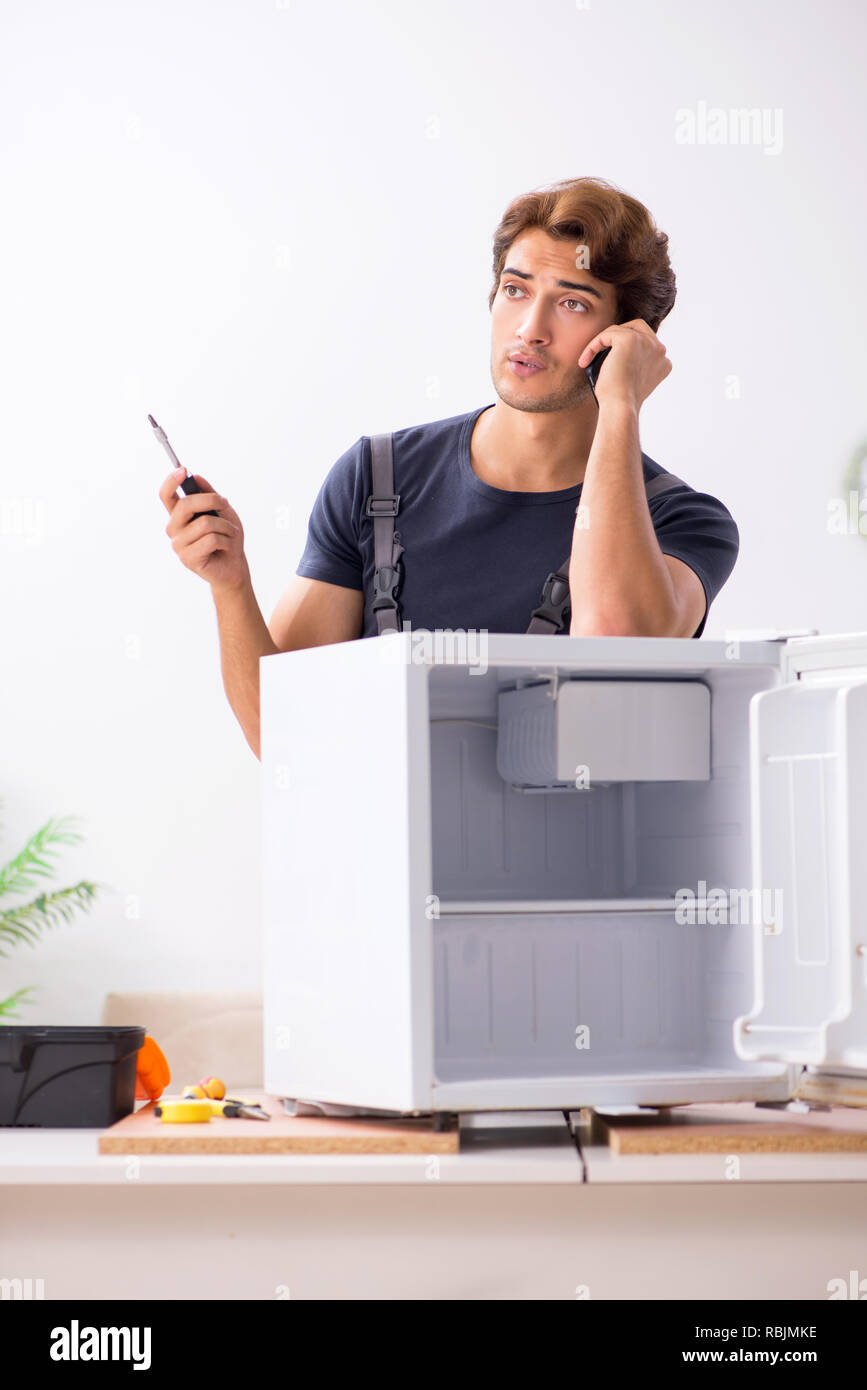 Young handsome contractor repairing fridge Stock Photo