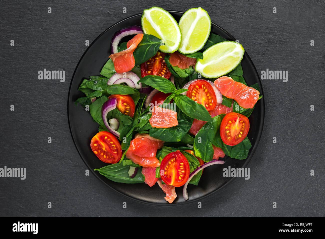 salmon salad with spinach, cherry tomatoes, red onion, lime and basil in black plate on black slate background. healthy food concept. top view Stock Photo