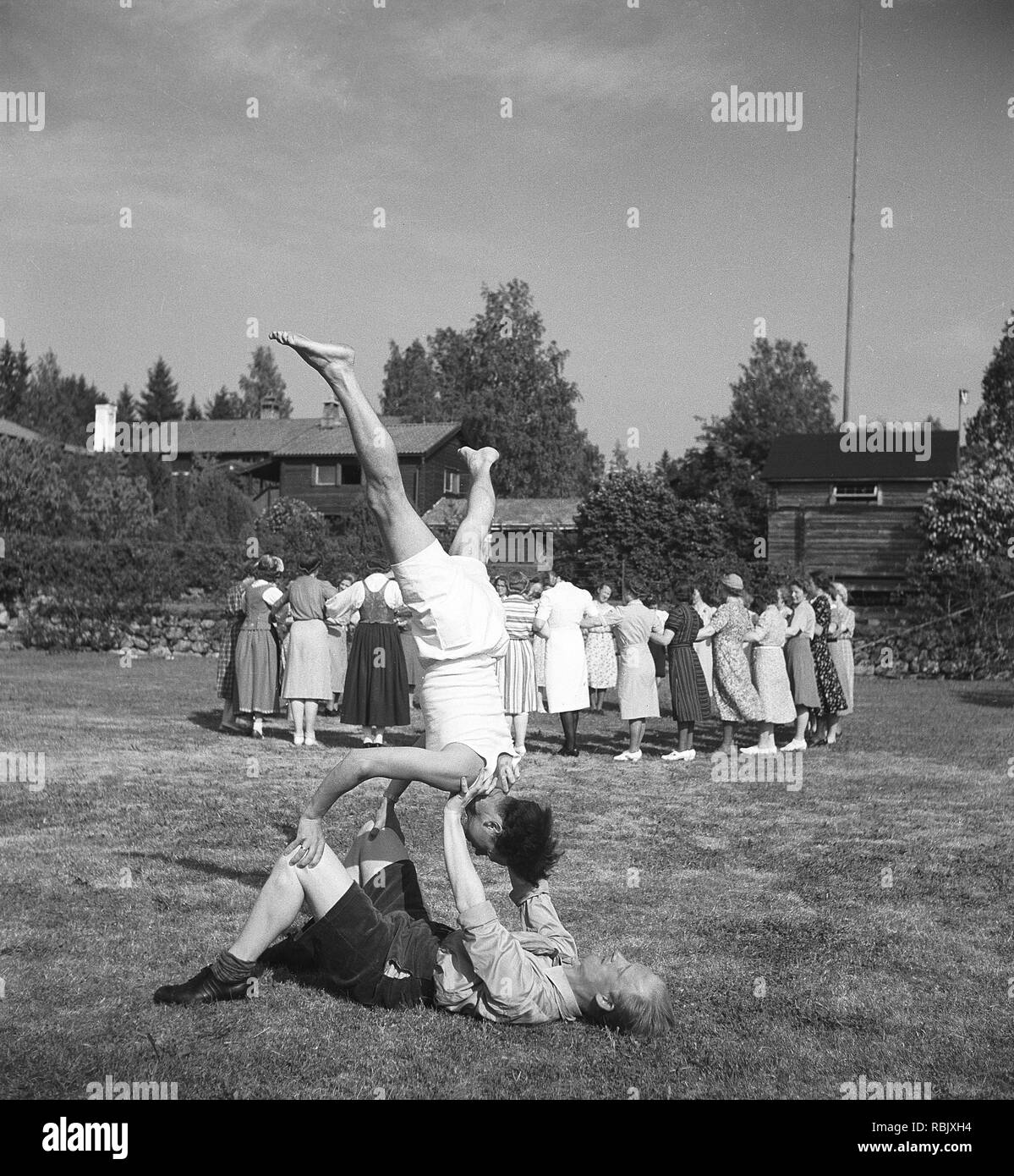 Summer dance in the 1940s. A group of women are practising their ring dance at an outdoor dance event in the summer. Two men in the forground does not appear interested in participating in that, and do their own balance act, unknown why. Photo Kristoffersson Ref 219-23. Sweden 1941 Stock Photo