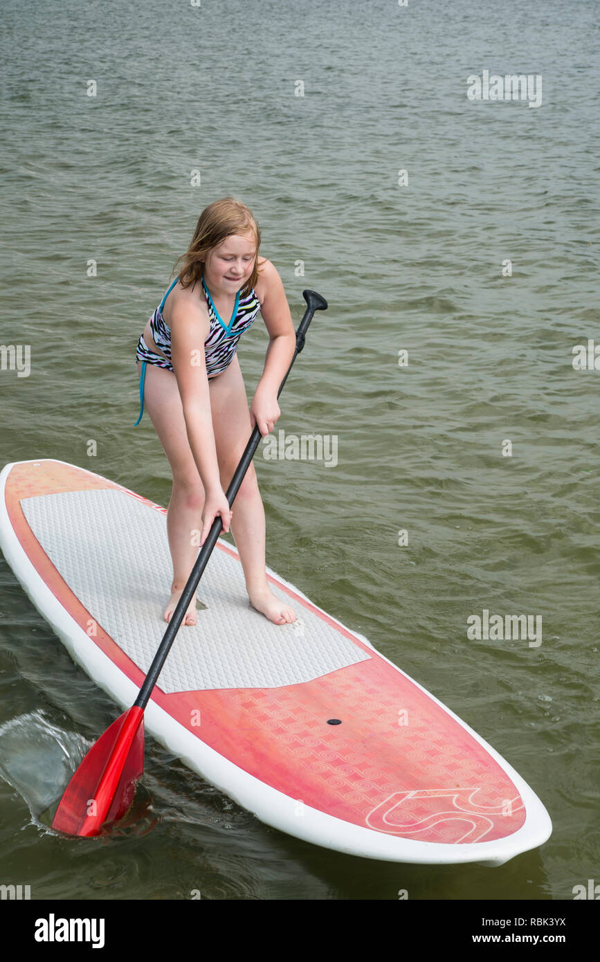 Naytahwaush; Minnesota. Nine year old girl paddle boarding on a lake. Stock Photo