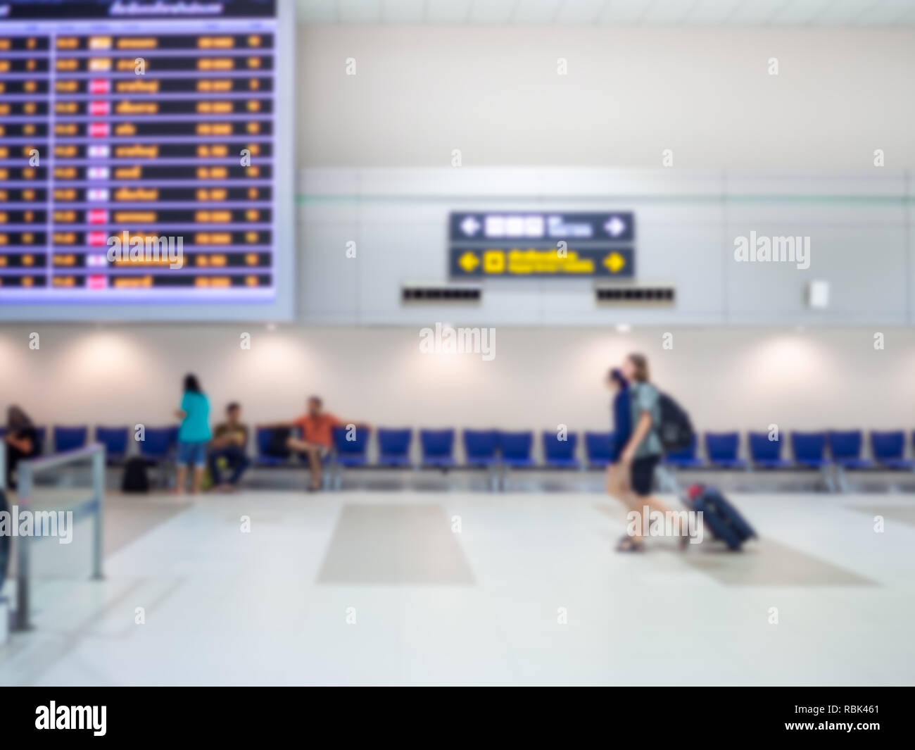 Blurred boarding time monitor screens and passengers in airport hall terminal interior area for arrival passenger. Stock Photo